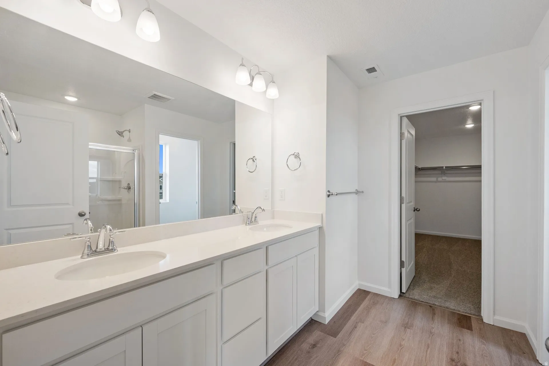 Primary bathroom with a walk-in closet, double vanity, a stall shower, and light wood-style flooring