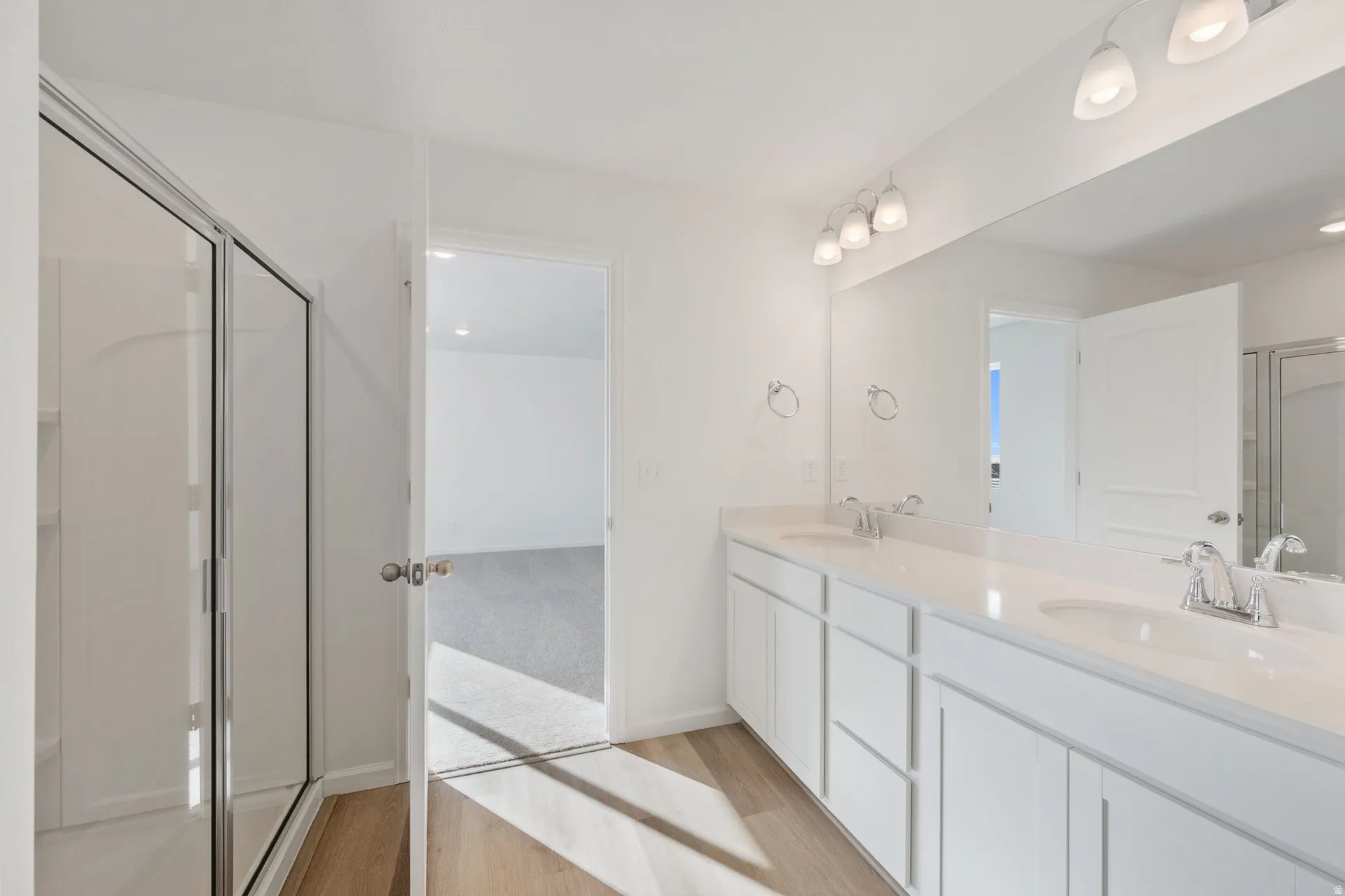 Primary bathroom with a shower stall, double vanity, and light wood-style floors