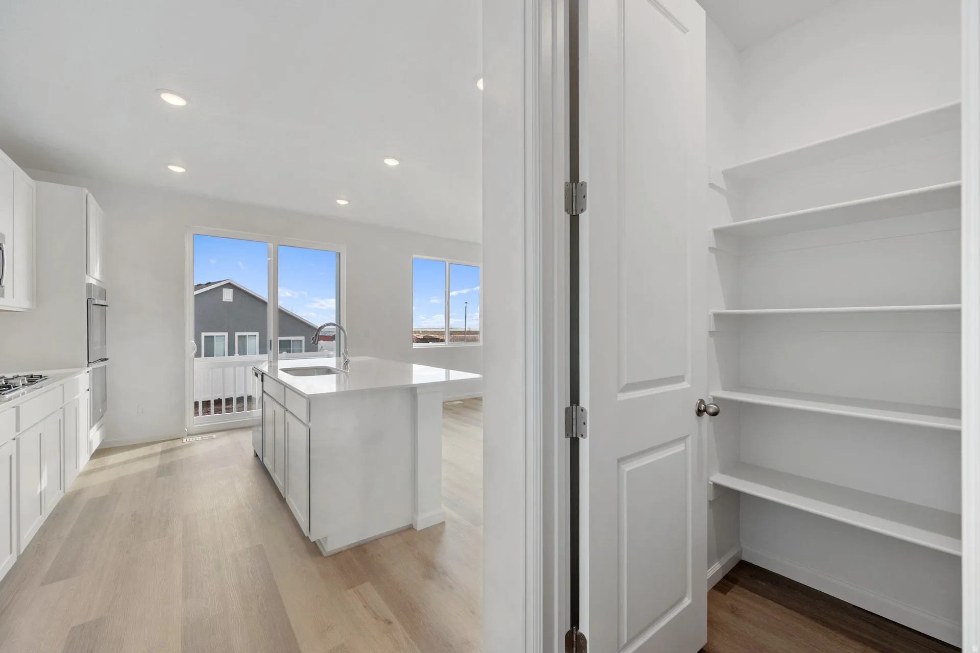Kitchen with an island with sink, white cabinetry, light wood finished floors, recessed lighting, light stone countertops, and walk-in pantry.