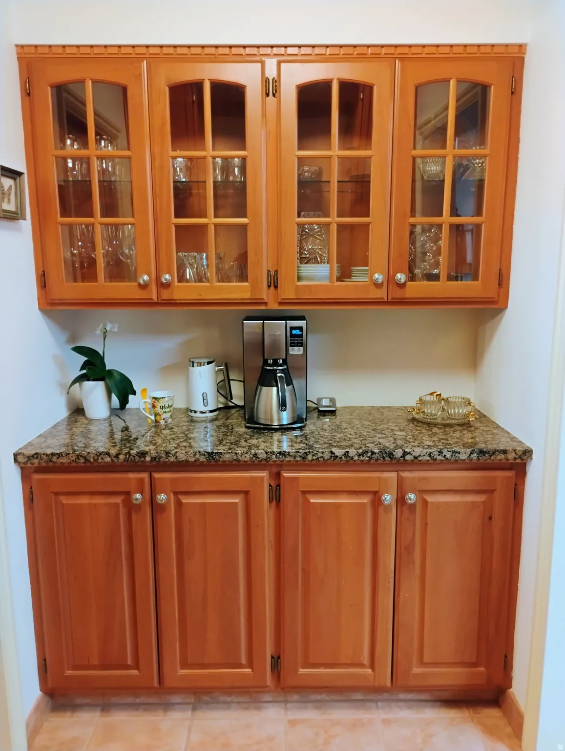 Bar area featuring glass insert cabinets, wood finish cabinetry, and dark stone countertops