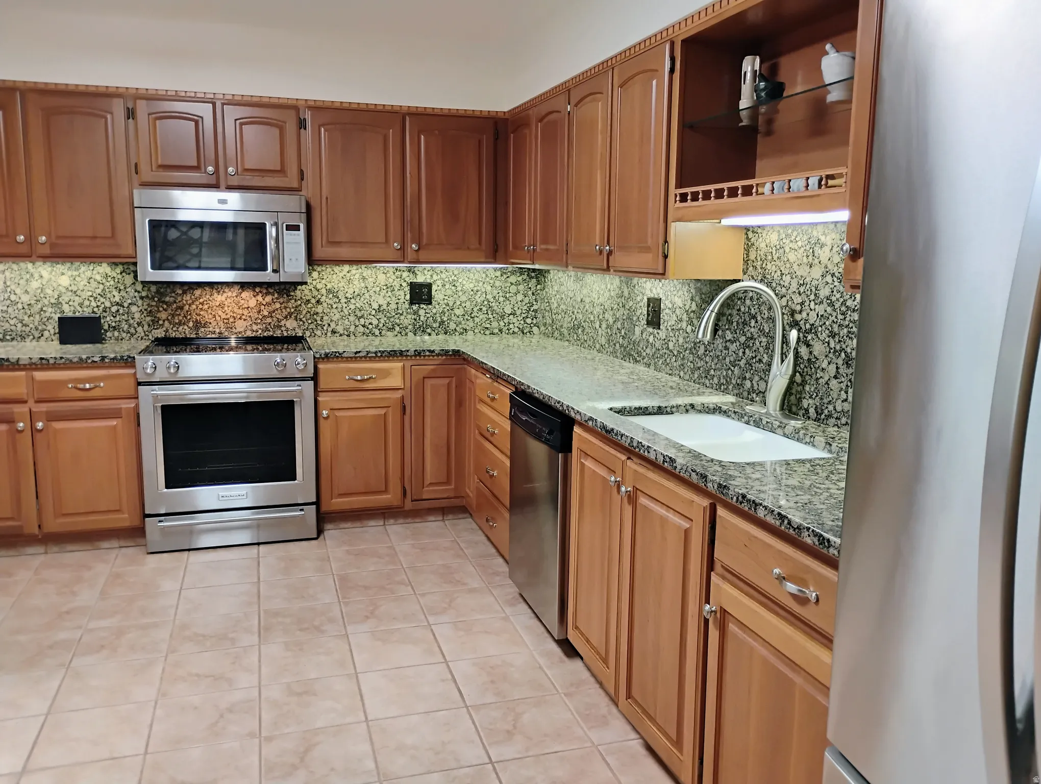 Kitchen featuring stainless steel appliances, wood finish cabinets, and dark stone counters