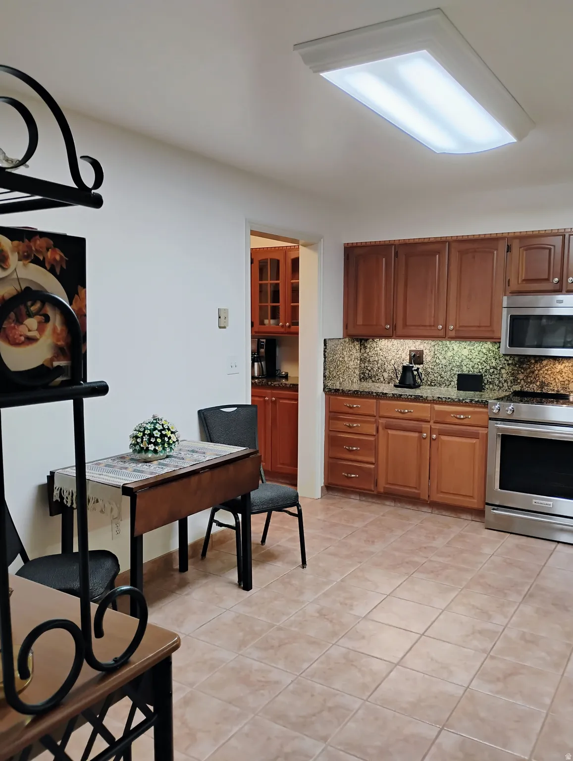 Kitchen featuring stainless steel appliances, dark stone countertops, wood finish cabinetry, backsplash, and light tile patterned floors