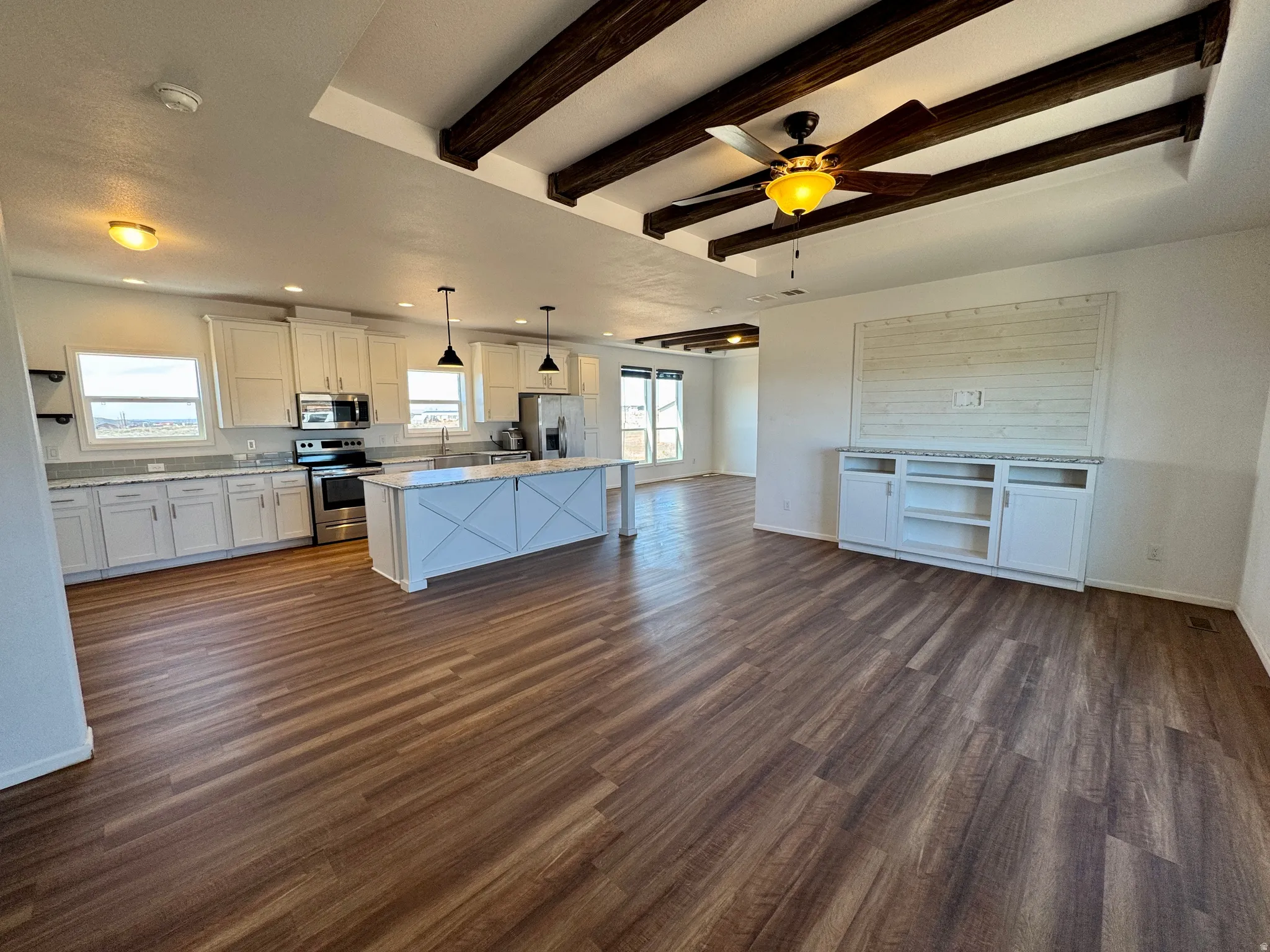 Kitchen featuring open floor plan, white cabinetry, beamed ceiling, stainless steel appliances, and a ceiling fan