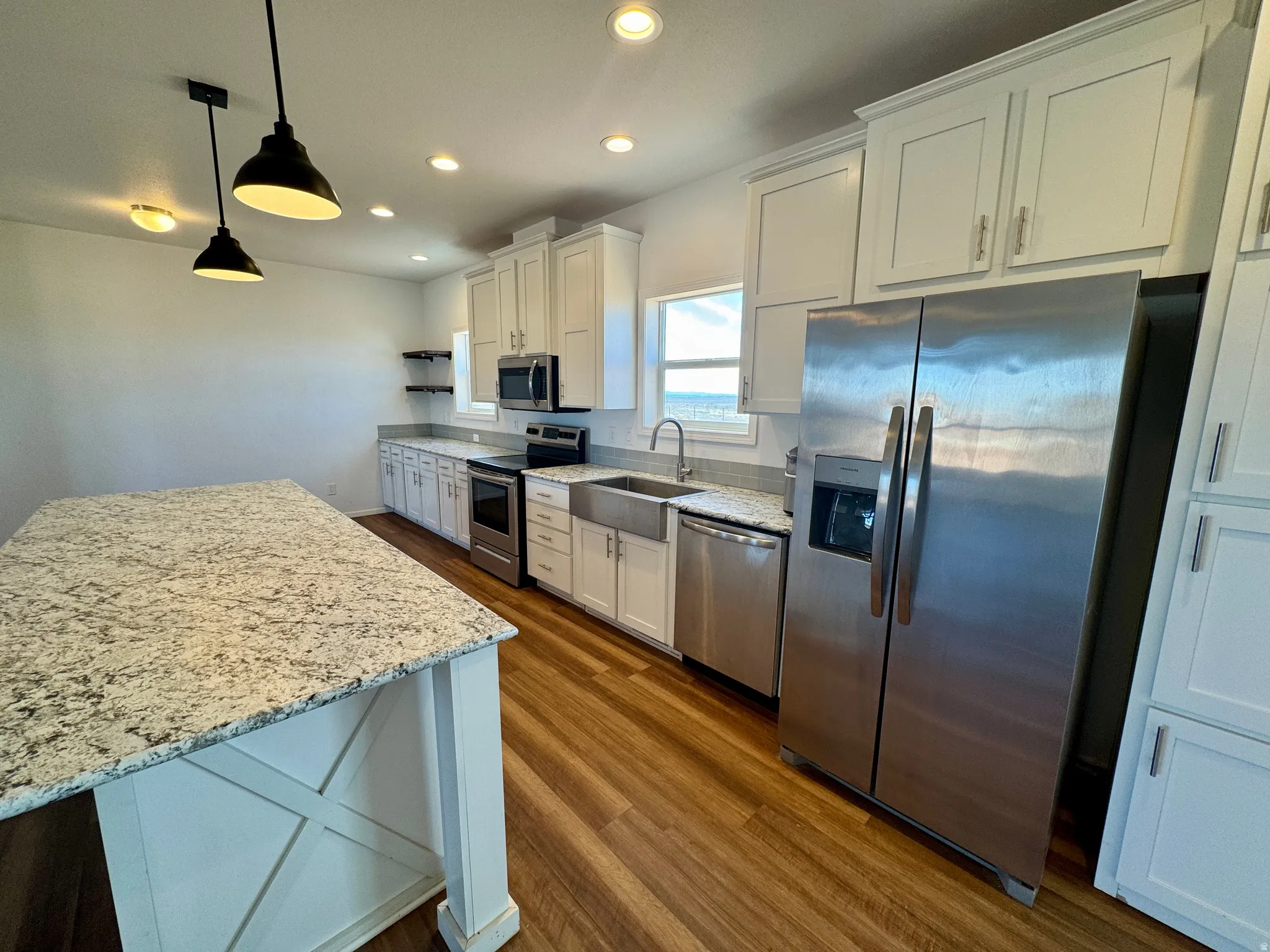 Kitchen with light stone countertops, stainless steel appliances, dark wood-style flooring, white cabinets, and hanging light fixtures