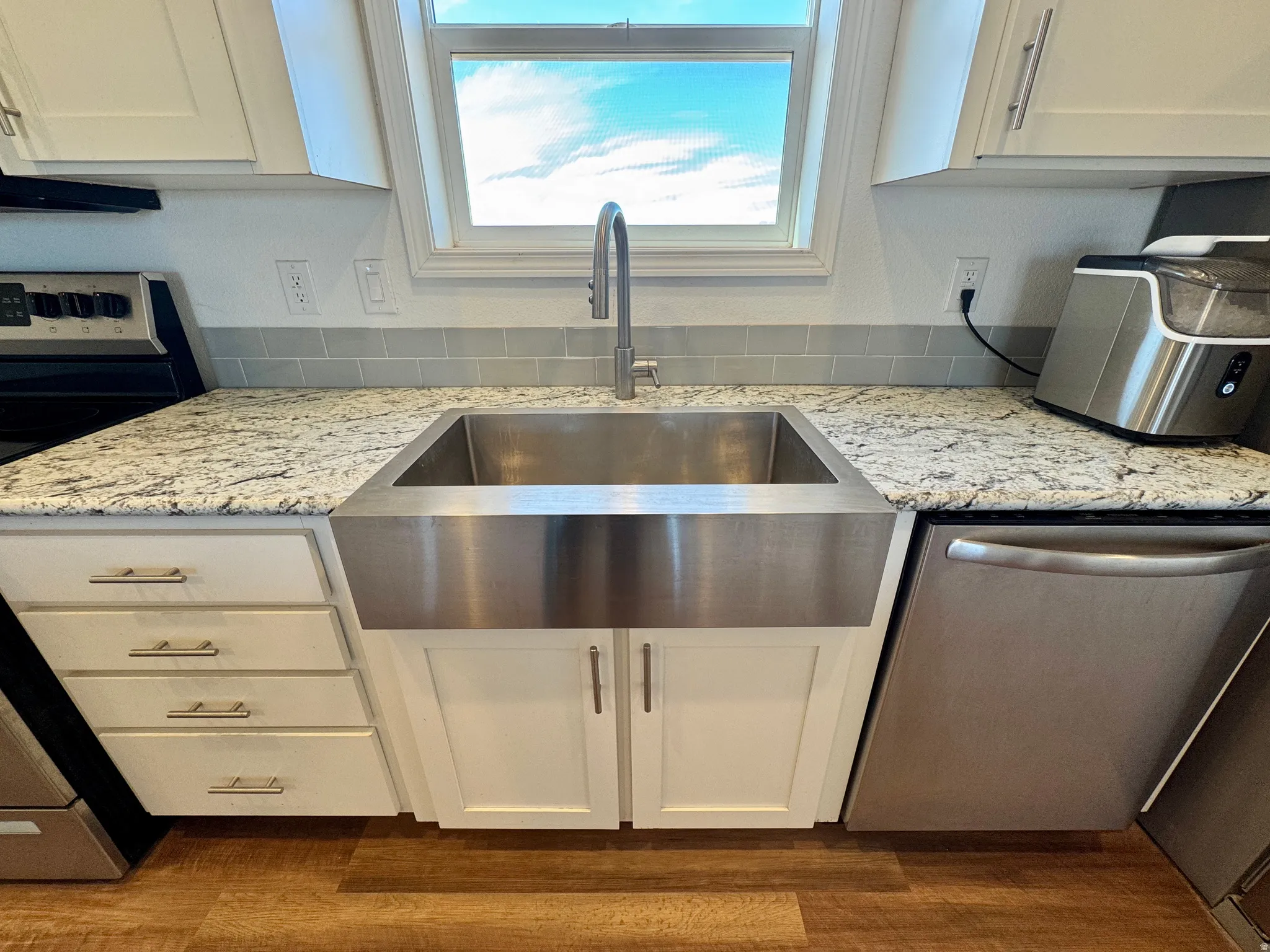 Kitchen featuring white cabinetry, light stone counters, stainless steel appliances, and dark wood finished floors