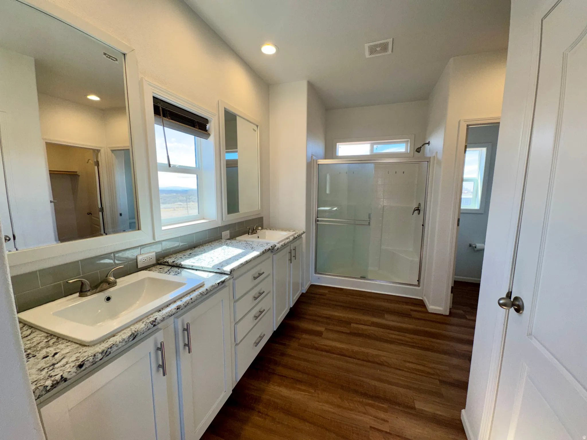 Ensuite bathroom with a shower stall, double vanity, dark wood finished floors, and decorative backsplash