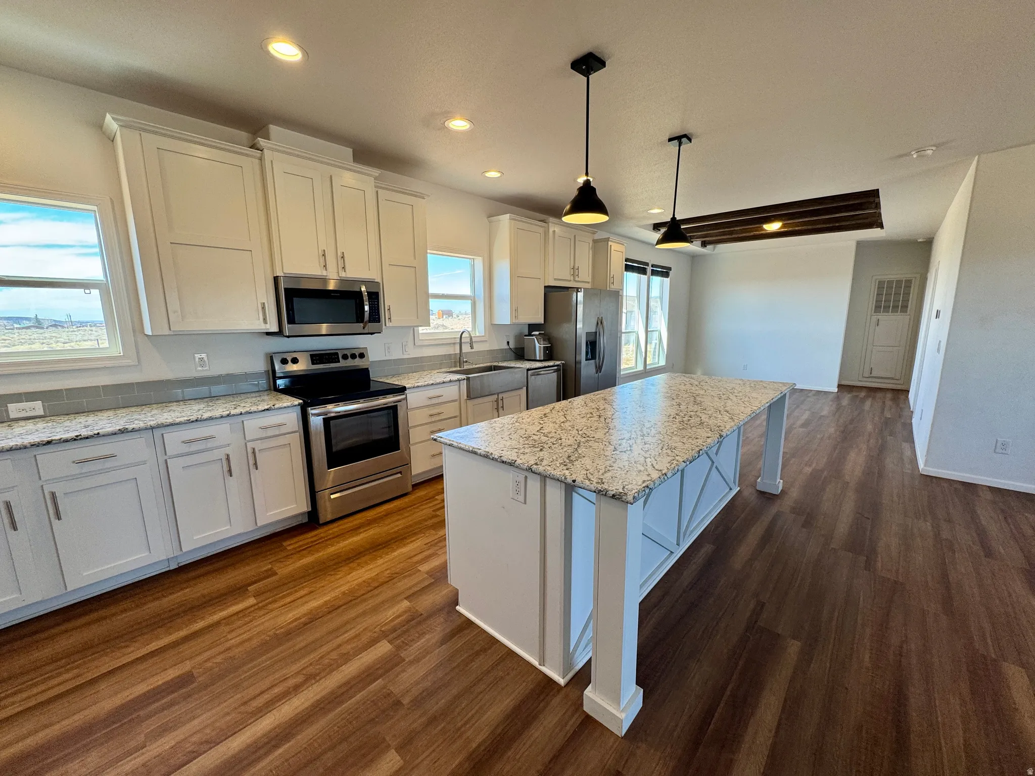 Kitchen with white cabinets, stainless steel appliances, a center island, light stone countertops, and dark wood-type flooring