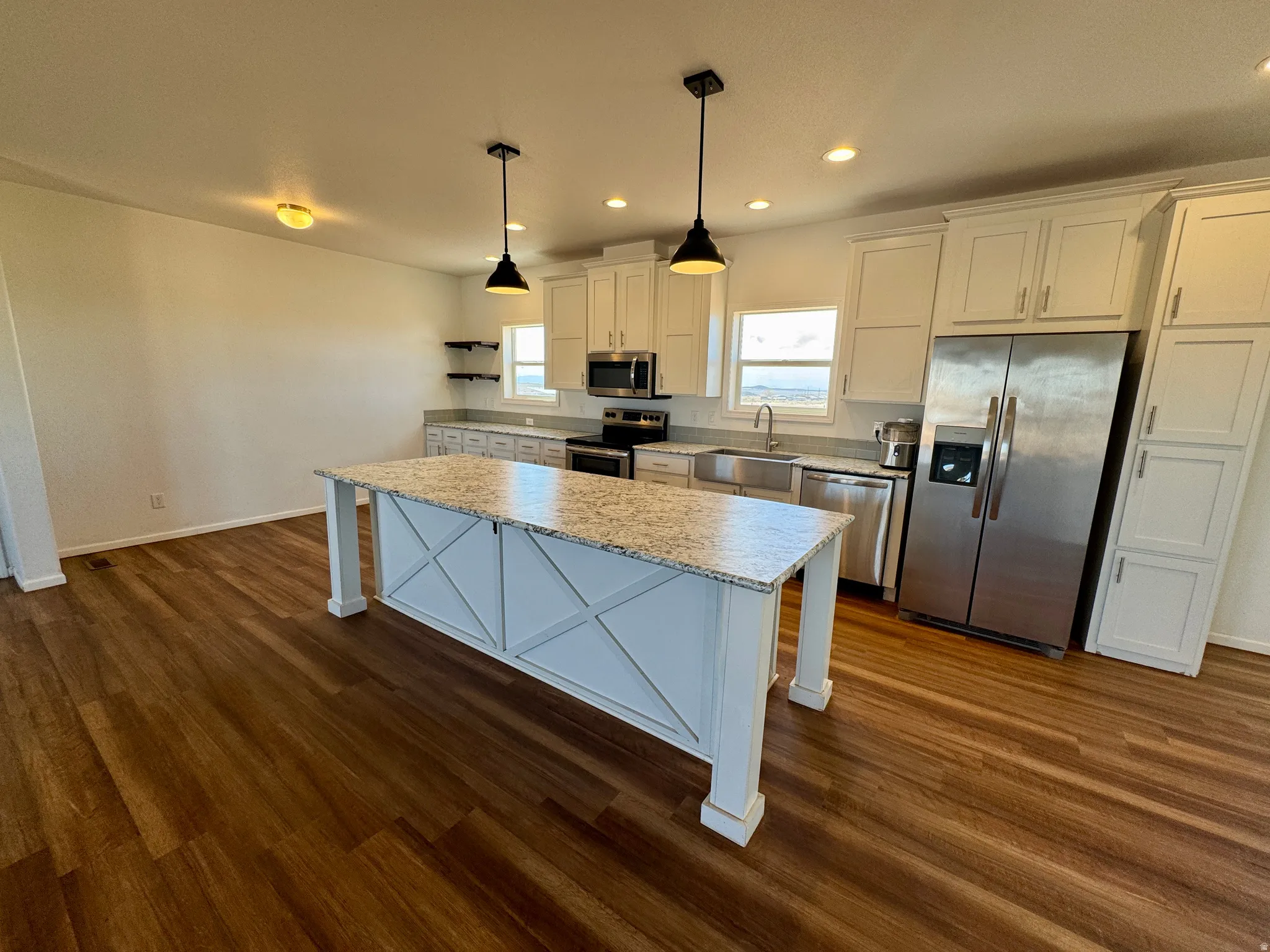 Kitchen featuring stainless steel appliances, white cabinets, hanging light fixtures, and plenty of natural light