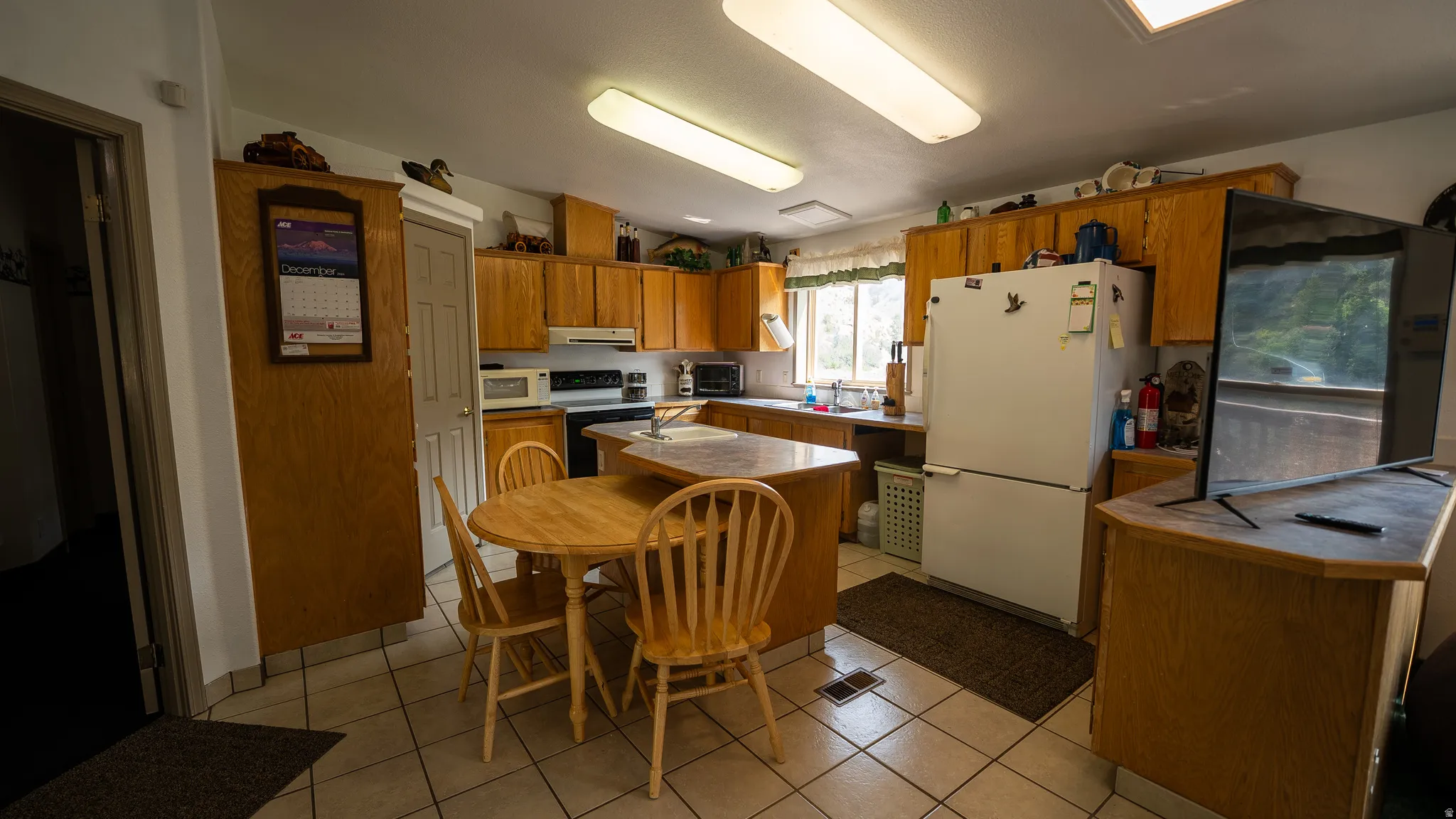 Kitchen featuring extensive light wood cabinetry, white appliances, and tiled flooring