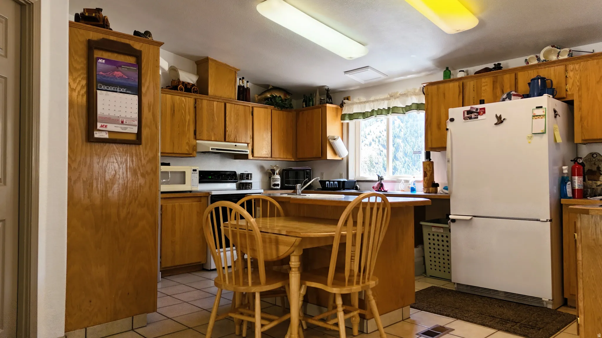 Kitchen featuring white appliances, wood finish cabinets, light countertops, and a breakfast bar area