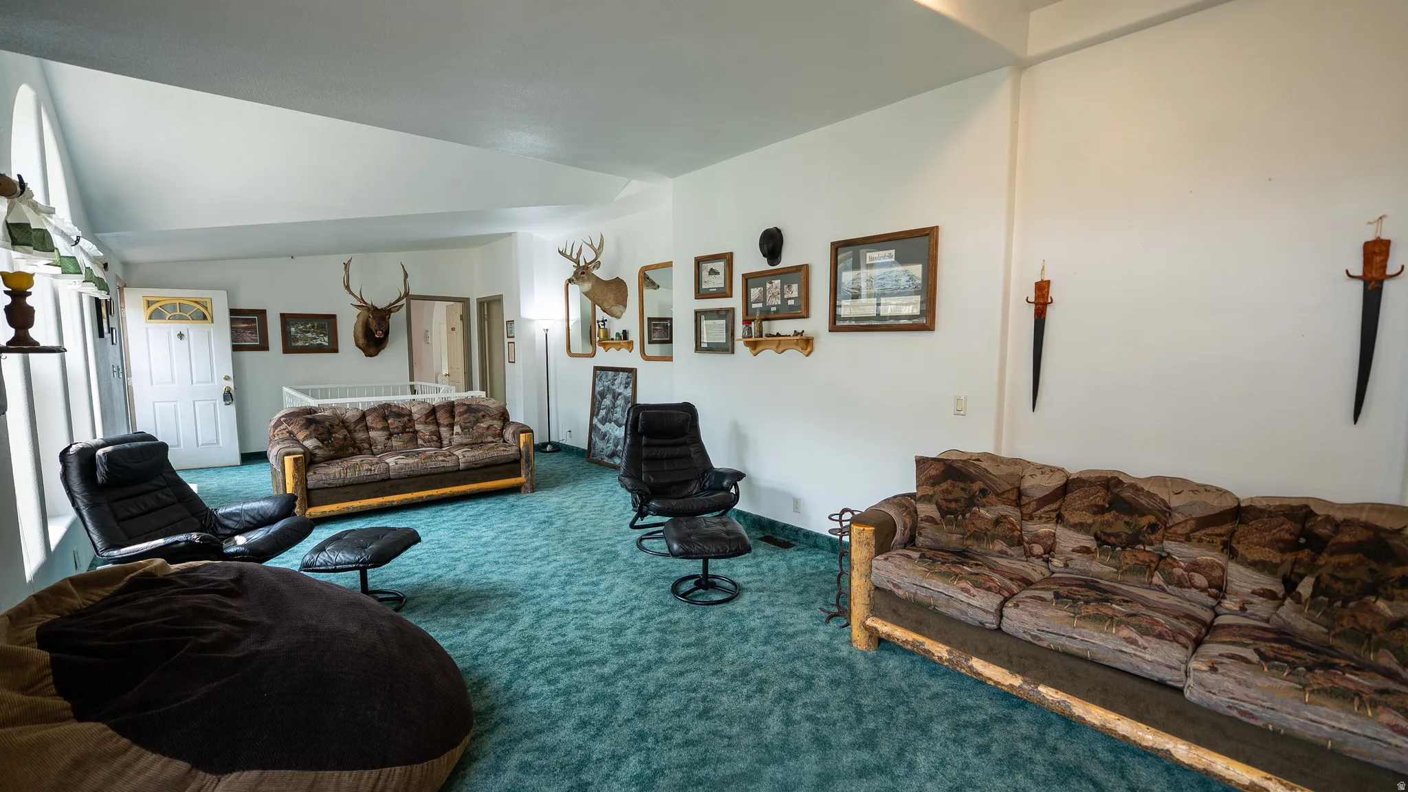 Spacious interior room featuring light blue carpeting, white walls, and a vaulted ceiling
