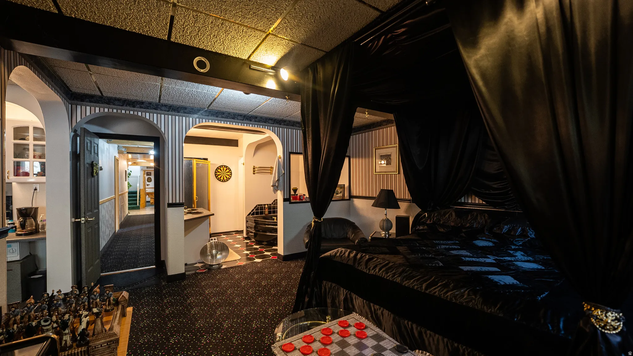 Recessed lighting illuminating a bedroom area with dark fabric canopy, accompanied by striped wallpaper accents, arched doorways, and a patterned carpet