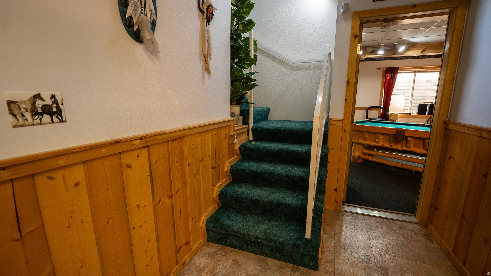 Hardwood wainscoting and green carpeted staircase leading to a spacious entertainment room with a pool table