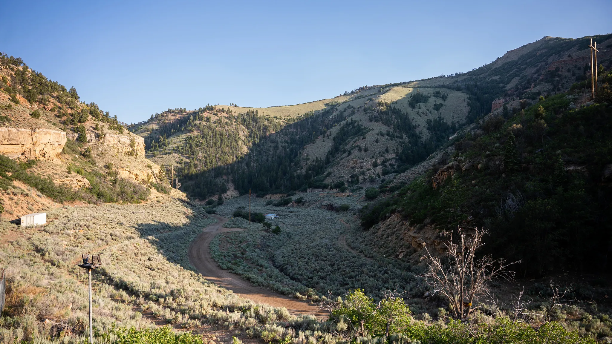 Expansive mountain landscape featuring varied terrain, a dirt road, and scattered structures