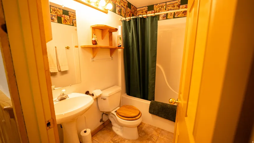 Bathroom featuring a pedestal sink, a toilet with a wood-finish seat, a shower/tub combination, and tiled flooring