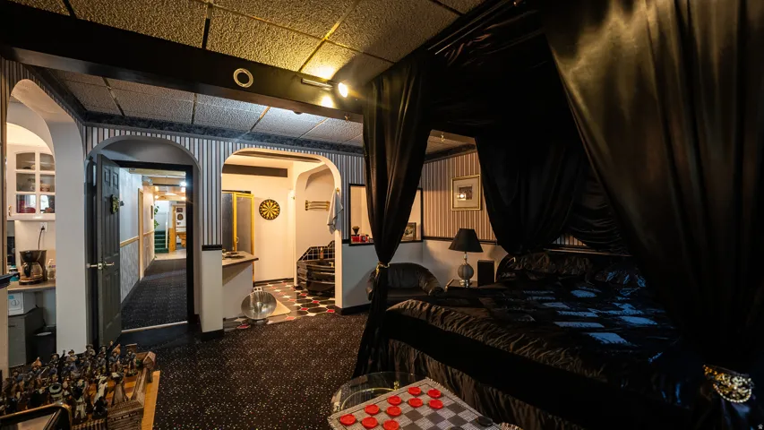 Recessed lighting illuminating a bedroom area with dark fabric canopy, accompanied by striped wallpaper accents, arched doorways, and a patterned carpet