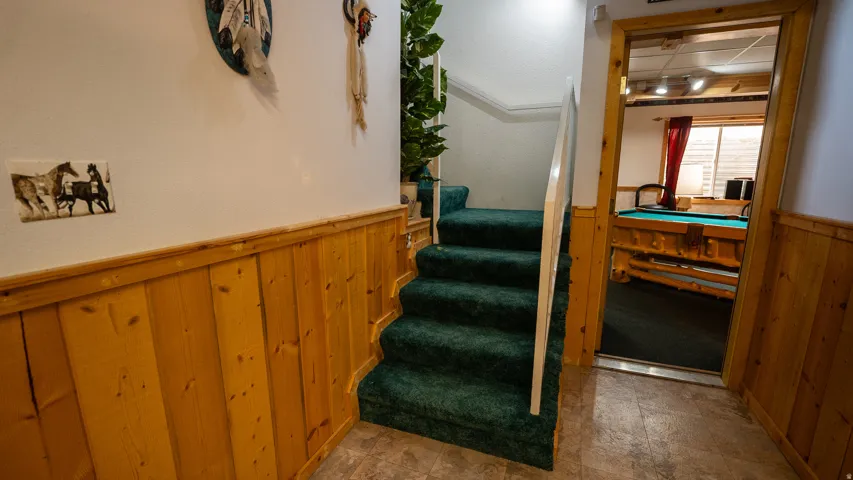 Hardwood wainscoting and green carpeted staircase leading to a spacious entertainment room with a pool table