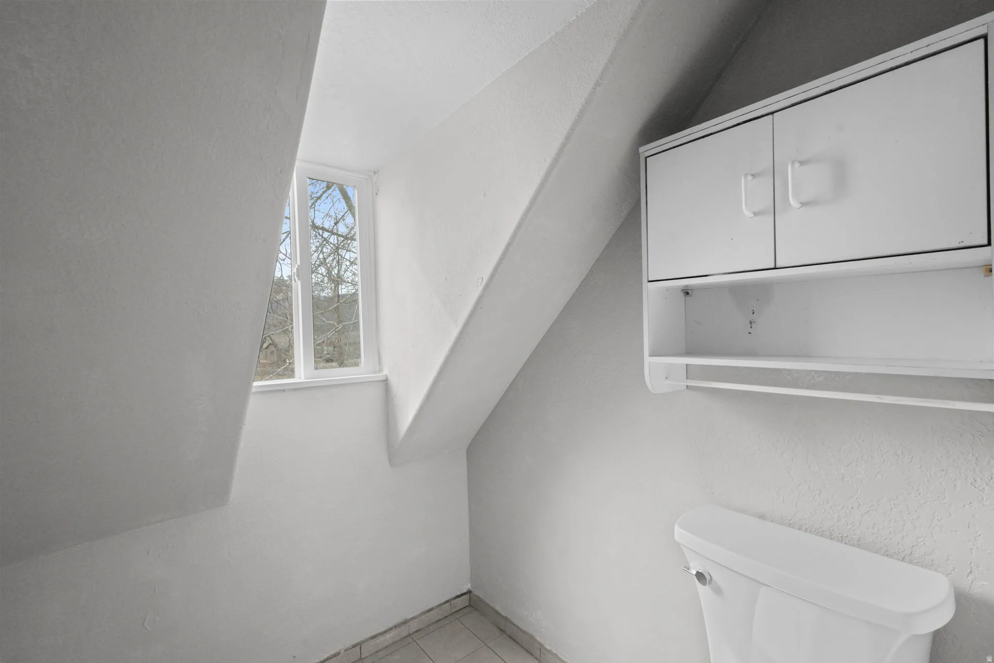 Half bath with a textured wall, lofted ceiling, and light tile patterned floors