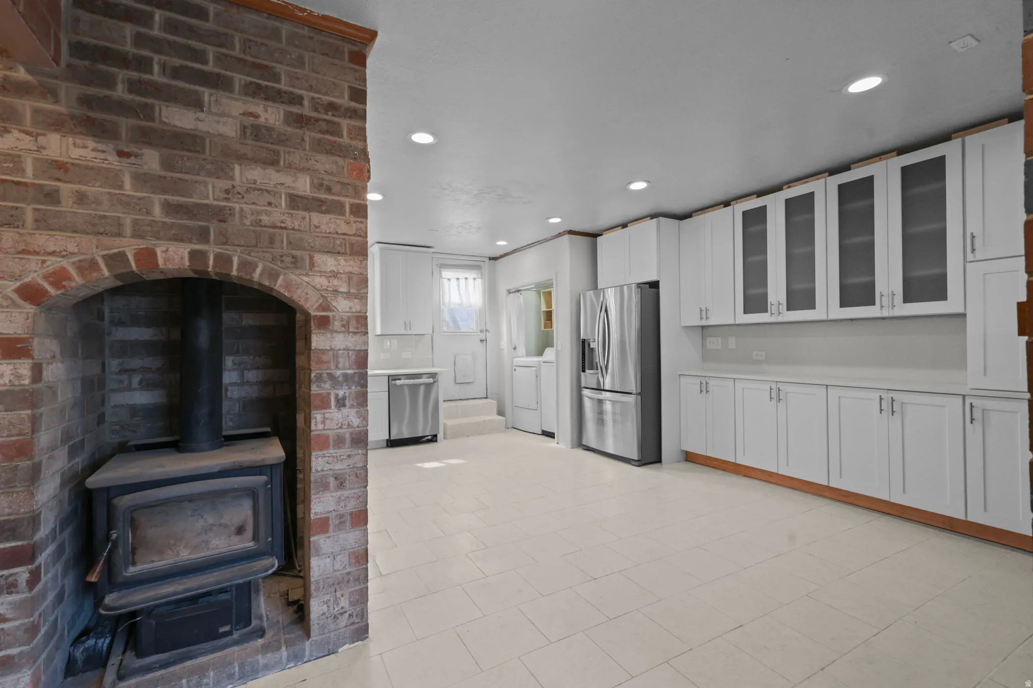 Kitchen featuring glass fronted cabinets, white cabinets, stainless steel appliances, recessed lighting, and a wood stove