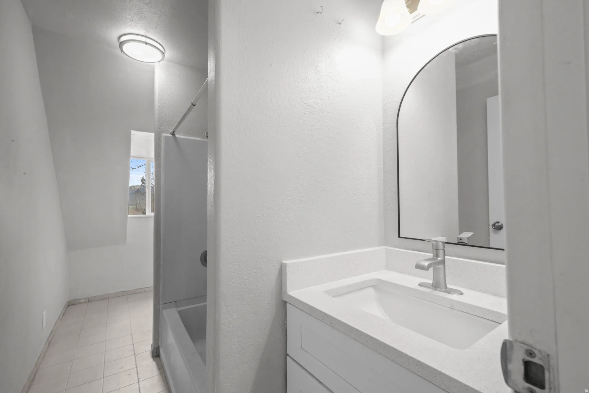 Bathroom with vanity, a textured wall, light tile patterned floors, and tub / shower combination