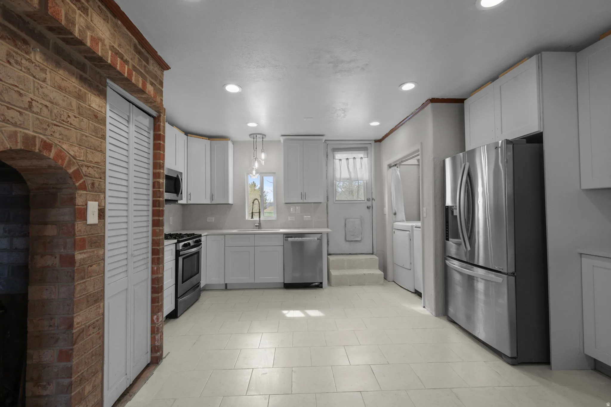 Kitchen featuring stainless steel appliances, backsplash, decorative light fixtures, and white cabinets