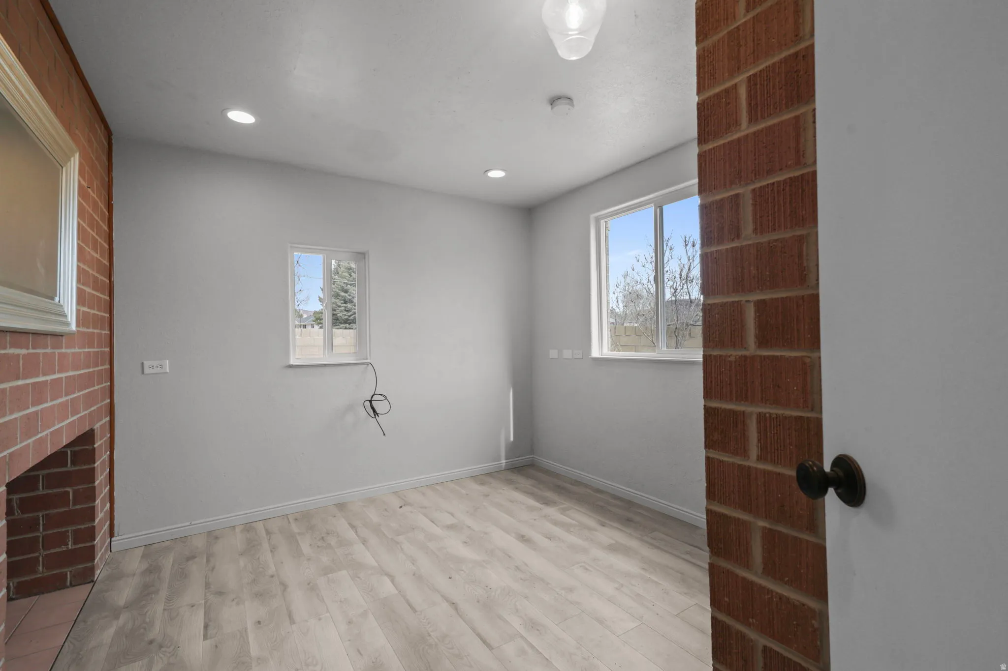 Empty room with light wood-style floors, brick wall, and recessed lighting