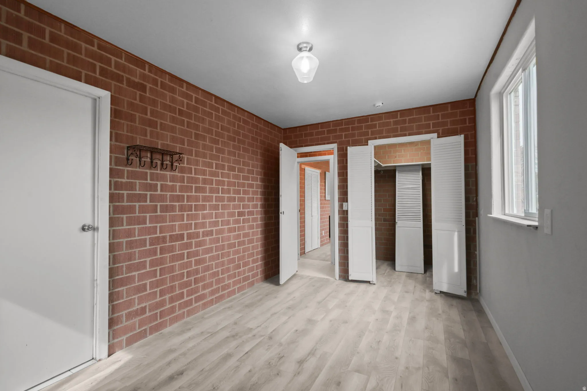 Unfurnished bedroom featuring light wood-type flooring, a closet, and brick wall