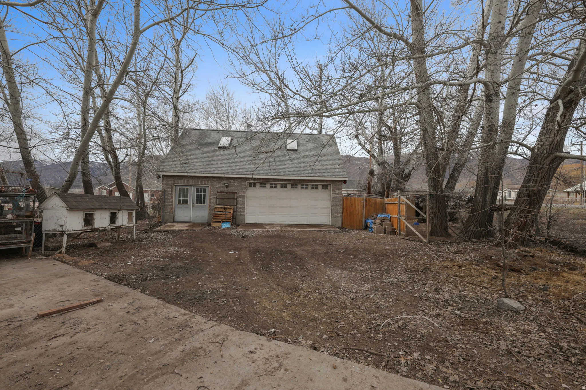 View of side of property with roof with shingles, a garage, driveway, an outbuilding, and brick siding