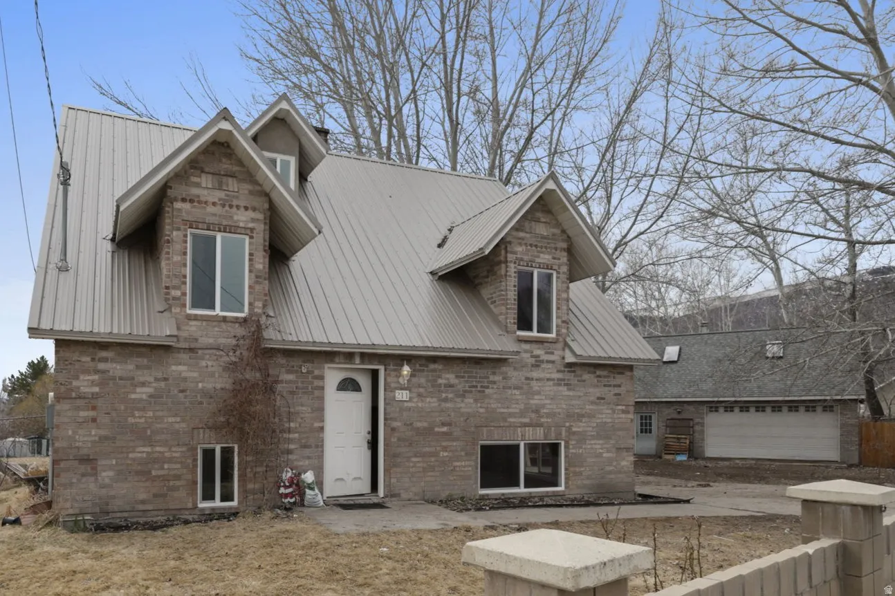 View of front of property featuring a metal roof, brick siding, a patio area, and a garage
