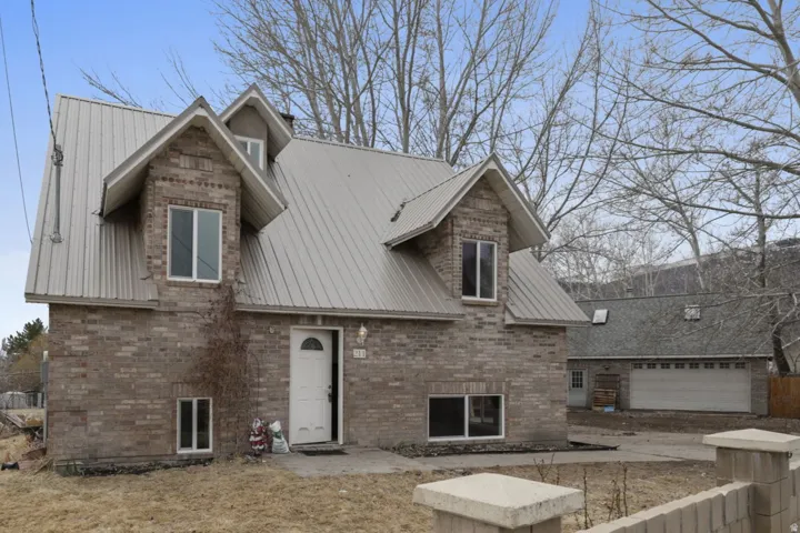 View of front of property featuring a metal roof, brick siding, a patio area, and a garage