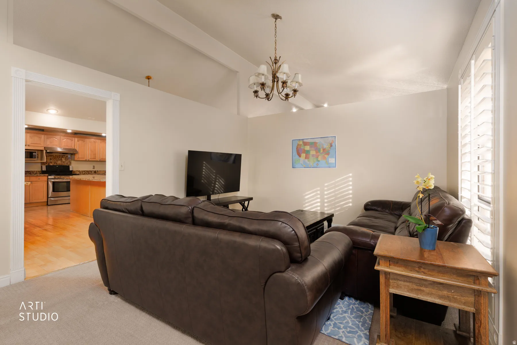 Living area with vaulted ceiling with beams, suspended lighting, and light carpet