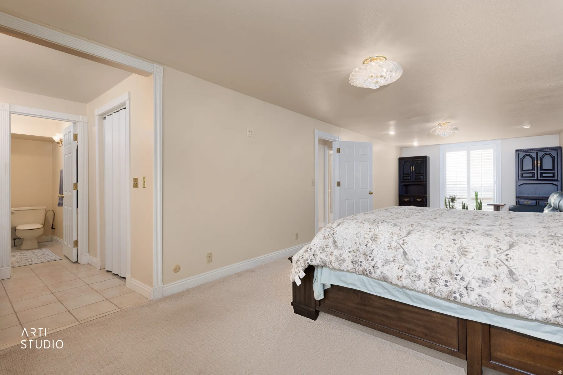Bedroom with light colored carpet, ensuite bath, and light tile patterned floors