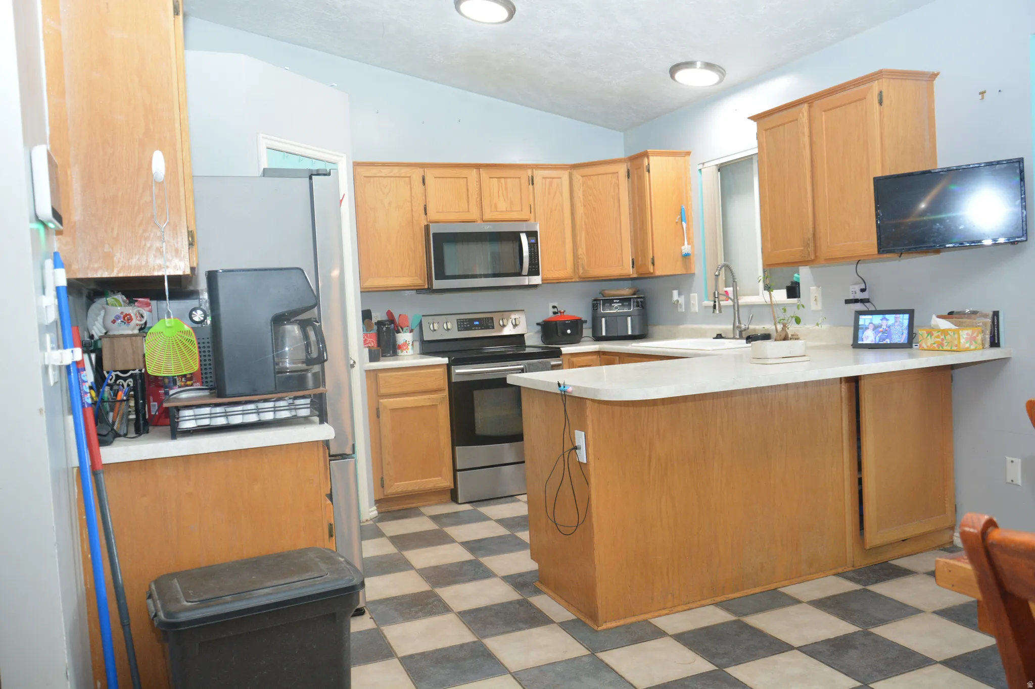 Kitchen featuring light flooring, a peninsula, light countertops, stainless steel appliances, and vaulted ceiling