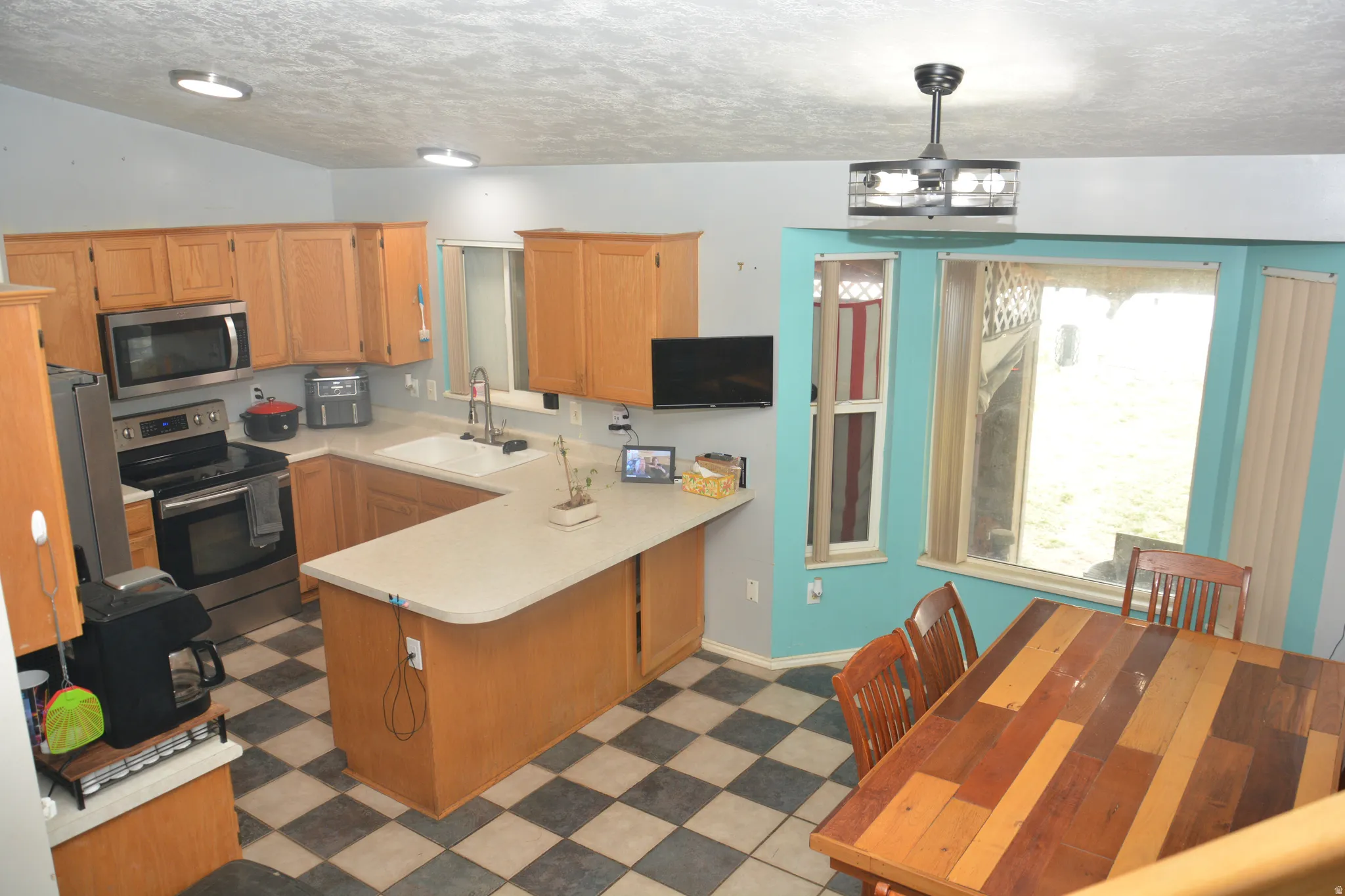 Kitchen with dark floors, stainless steel appliances, a peninsula, light countertops, and a textured ceiling