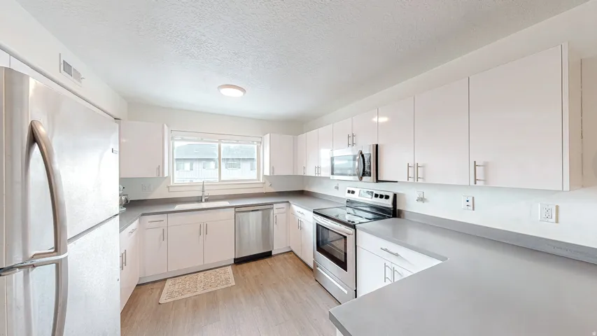 Kitchen with stainless steel appliances, a textured ceiling, white cabinets, light wood-type flooring, and light countertops