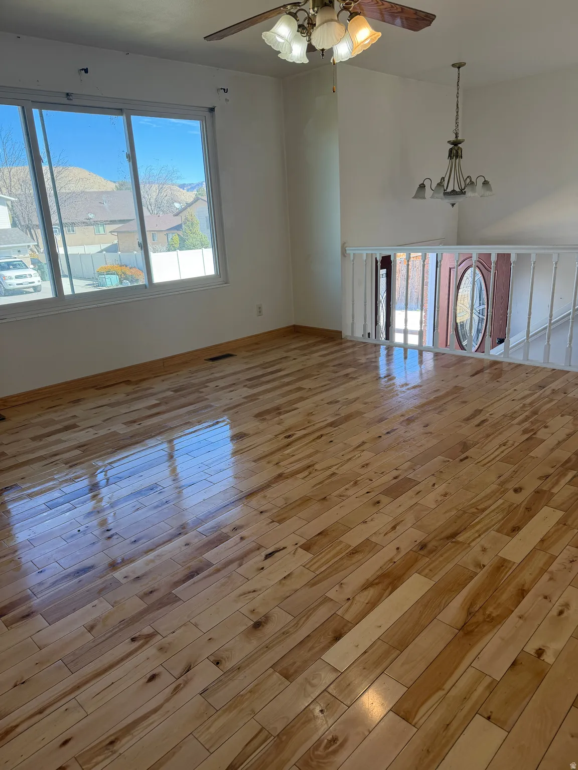 Empty room with a ceiling fan, light wood-style floors, and a chandelier