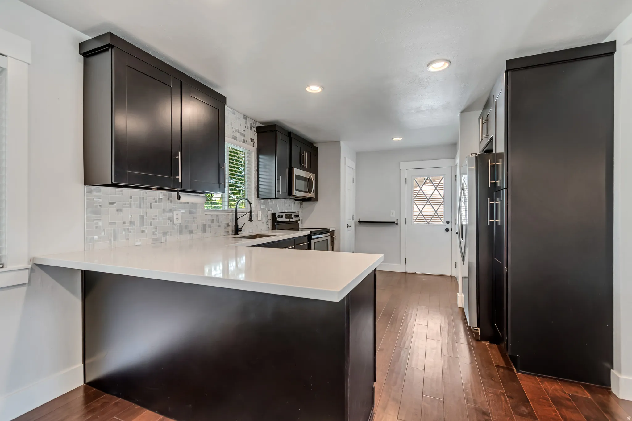 Kitchen featuring dark cabinetry, white countertops, a mosaic tile backsplash, stainless steel appliances, and wood-finish flooring