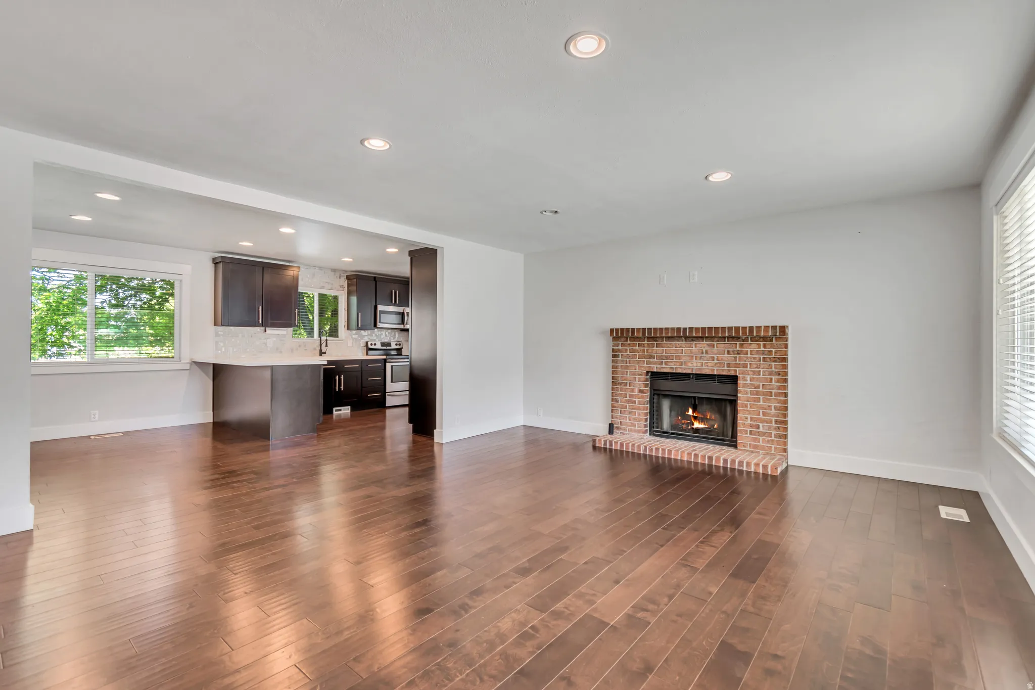 Open-concept living space featuring wood-finish flooring, a brick fireplace, and recessed lighting