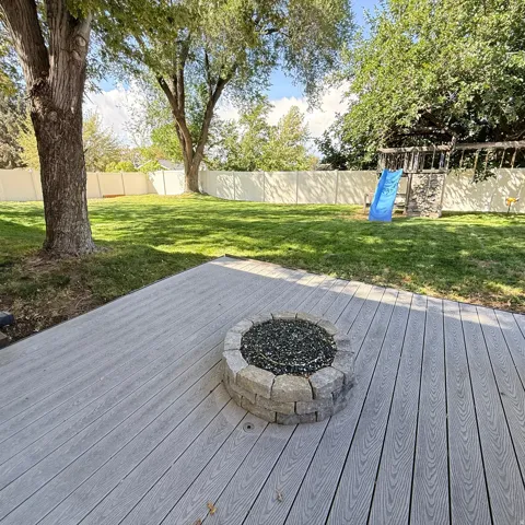 Expansive backyard with a composite deck, built-in stone fire pit, and mature trees