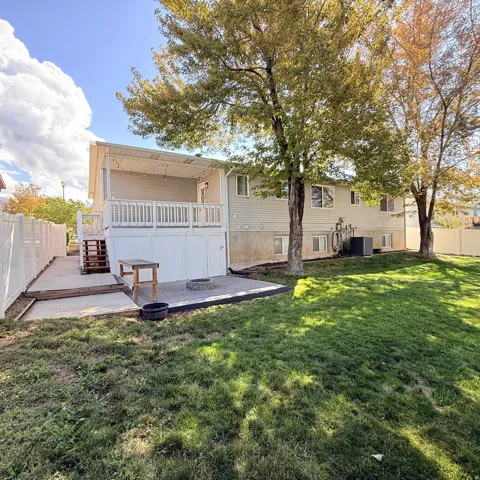 Expansive backyard featuring a covered deck, lower patio with fire pit, and white privacy fencing