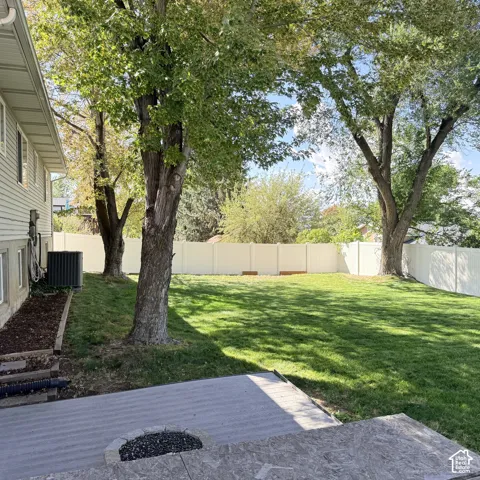 Expansive backyard featuring a manicured lawn, established trees, and a durable vinyl fence
