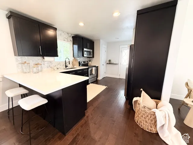 Modern kitchen featuring dark wood-finish flooring, white countertops, black cabinetry with brushed nickel hardware, a tile backsplash, and stainless steel appliances
