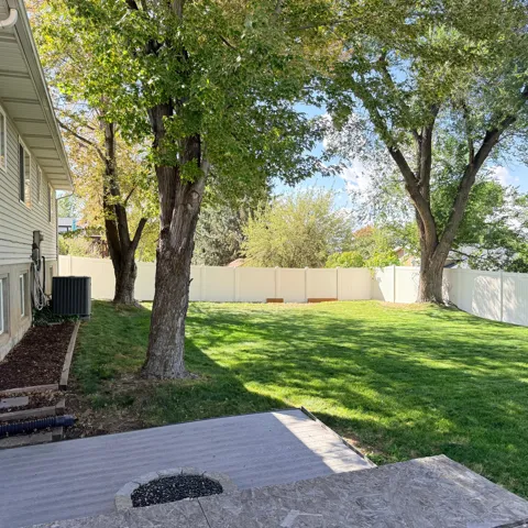 Expansive backyard featuring a manicured lawn, established trees, and a durable vinyl fence