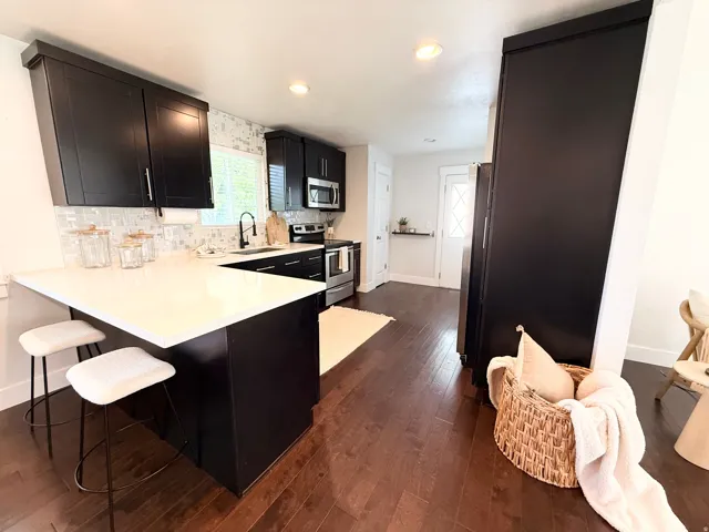 Modern kitchen featuring dark wood-finish flooring, white countertops, black cabinetry with brushed nickel hardware, a tile backsplash, and stainless steel appliances