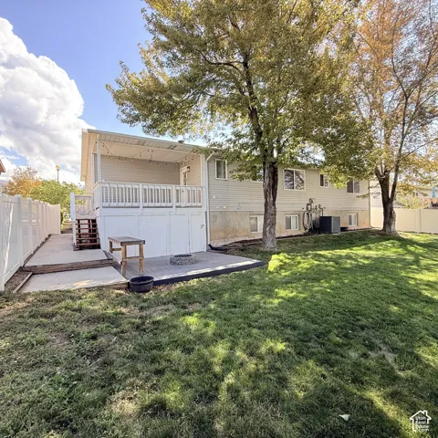 Expansive backyard featuring a covered deck, lower patio with fire pit, and white privacy fencing