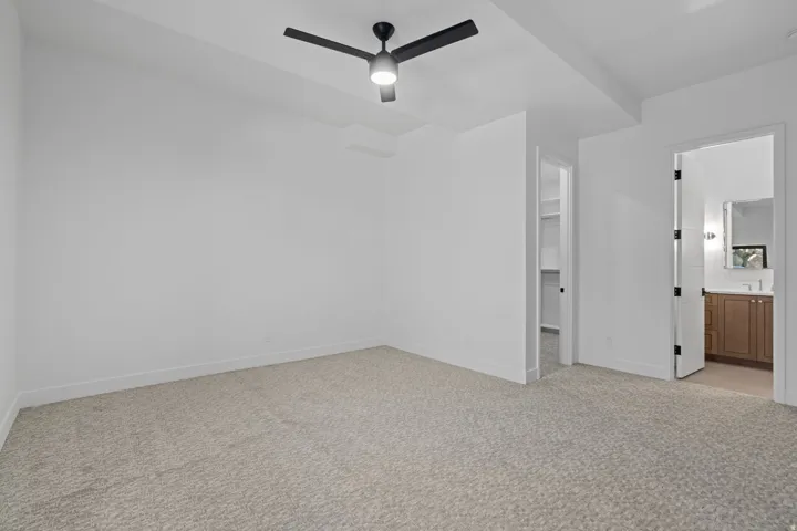 ADU bedroom suite with light carpet, a walk in closet, a ceiling fan, and ensuite bath