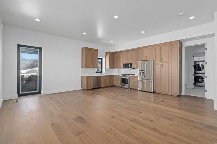 ADU Kitchen featuring stainless steel appliances, light countertops, stacked washer / dryer, tasteful backsplash, and light wood-style floors