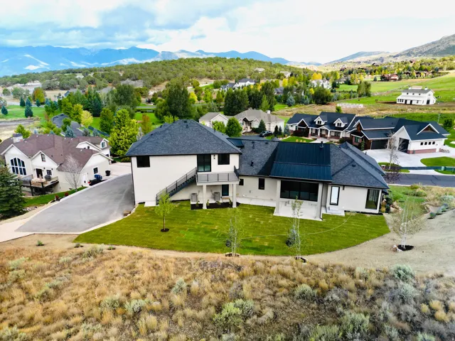 Modern two-story residence with white stucco exterior, dark shingle and metal roofing, and a lower-level patio