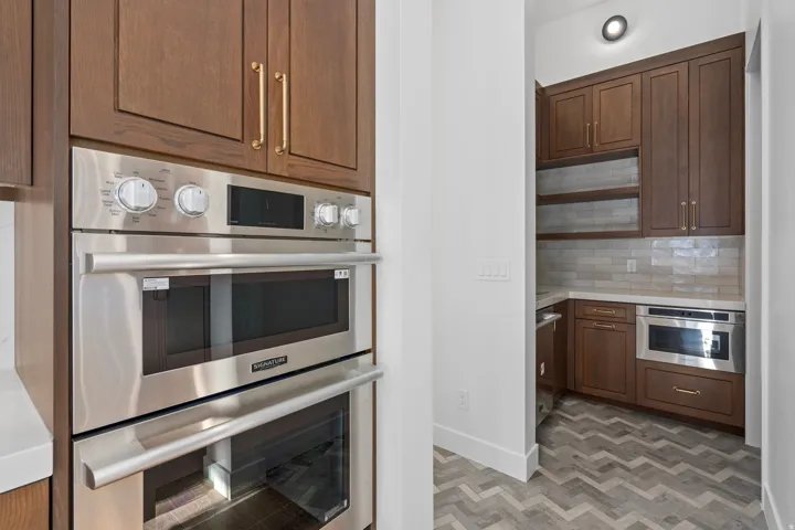 Kitchen featuring stainless steel double oven, backsplash, light stone countertops, dark wood finish cabinets, and open shelves