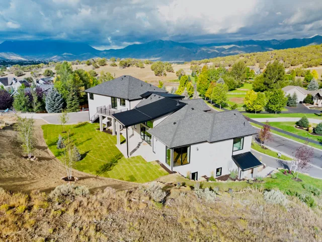 Modern architecture with a light-toned facade, dark-pitched roofs, extensive window placements, a covered patio, and terraced landscaping with newly laid sod